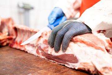 Close up view of butcher's hands wearing metal protection glove and cutting raw meat with sharp...
