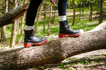 Close-up of hiker's feet carefully stepping on fallen tree trunk, showcasing stylish black boots with red soles while navigating forest path