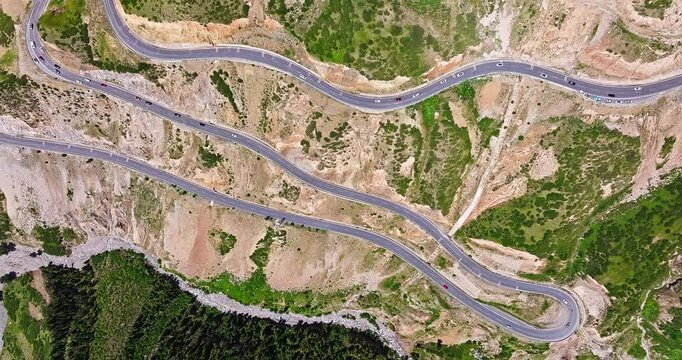 Aerial view of a winding mountain road with cars navigating the hairpin turns and curves