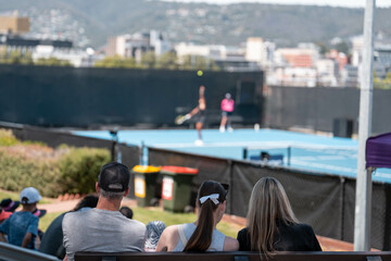 Female tennis player playing social tennis on a blue tennis court holding a tennis racket and wearing a hat
