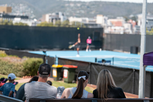 Female tennis player playing social tennis on a blue tennis court holding a tennis racket and wearing a hat