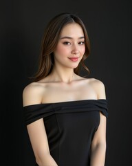 Naklejka premium A woman poses confidently in an off-shoulder black outfit against a dark background, exuding elegance and charm.
