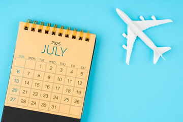 July 2025 calendar and airplane toy on blue background.