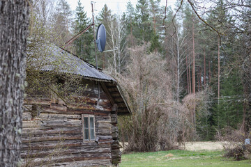 
An old, wooden building with a satellite dish on the roof, located in a wooded area.