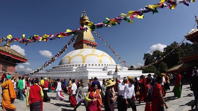 Devotees participate in a spiritual pilgrimage around Boudhanath Stupa, showcasing vibrant cultural traditions under a bright blue sky