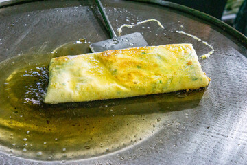 Chef is cooking egg martabak, a traditional Indonesian food. Vegetables, meat, and various other spices are wrapped in a thick dough skin which is thinned and then fried