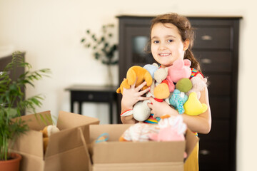 Happy cute little kid girl having fun after moving into a new home. Child with cardboard boxes with...