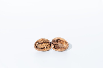 A walnut split in half on a white background. Half of the shell contains the fruit, while the other...