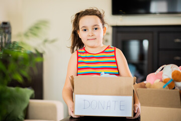 Cute teenager kid girl packing cuddly toys in the donation box at home.