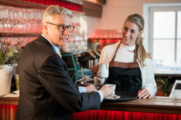 Smiling barista in an apron hands a steaming cup of coffee to a customer, providing excellent service in a café