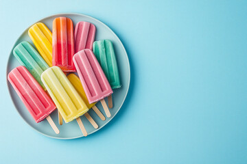 bright popsicles on a stick with different flavors on a round plate on a blue background with space for copying text
