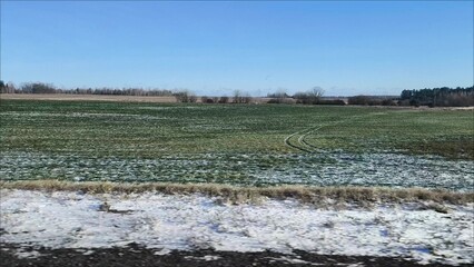 Spring landscape from the car window. There is snow on the fields in places, and the sky is clear and blue. travel view from the car window on a early spring. green fields are covered with snow in pla