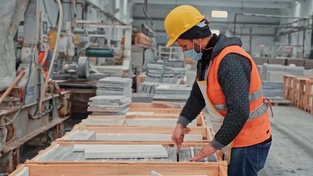 Production line in a stone processing facility. Workers wearing protective gear inspect and prepare marble slabs for packaging.
