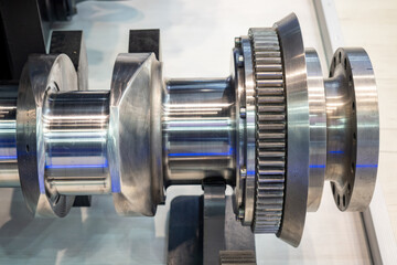 A polished metal crankshaft or mechanical component with precisely machined surfaces and gear...