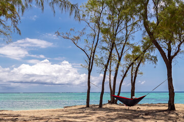 Paradise awaits: hammock between casuarina trees on tropical beach.Red hammock by turquoise waters.Coastal retreat