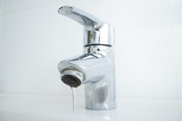 Close up of a bathroom faucet with running water and limescale stains and dirty sink