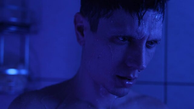 Exhausted man standing under shower, deep in thought after an emotionally draining day, surrounded by blue light. A cinematic mood. Depression and disappointment with life. On the verge of suicide