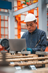 A professional engineer is working seriously on a laptop to check the metal sheet production in a factory. Focused on machinery, he ensures manufacturing quality in the industry.