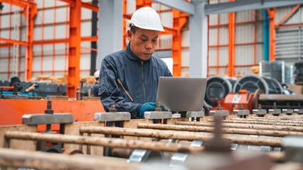 A professional engineer is working seriously on a laptop to check the metal sheet production in a factory. Focused on machinery, he ensures manufacturing quality in the industry.