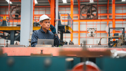 A professional engineer is working seriously on a laptop to check the metal sheet production in a factory. Focused on machinery, he ensures manufacturing quality in the industry.