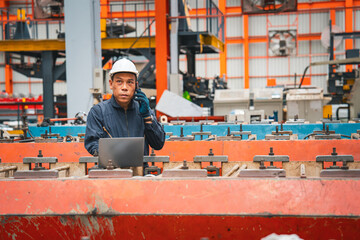 A professional engineer is working seriously on a laptop to check the metal sheet production in a factory. Focused on machinery, he ensures manufacturing quality in the industry.