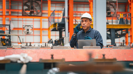 A professional engineer is working seriously on a laptop to check the metal sheet production in a factory. Focused on machinery, he ensures manufacturing quality in the industry.