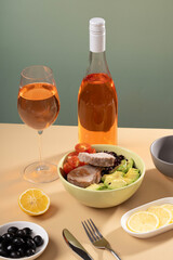 A bowl of tasty tuna and vegetable salad, a glass of wine, a modern naturism on a coloured table, flat plan. Place for text