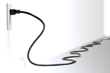 Long black electrical cord plugged into amarican us outlet and snaking off into distance