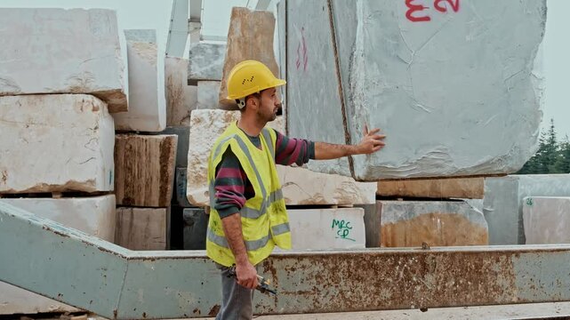 Crane operator guiding stone blocks in a marble quarry. A worker controls the movement of large stone blocks using a remote control.