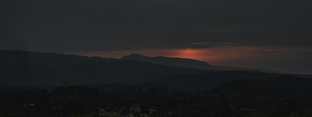 The red sunrise paints the early morning with a warm sunrise glow at dawn. Above, the gray sky looms with an overcast, creating a cloudy sky that adds to the dramatic sky and its natural beauty.