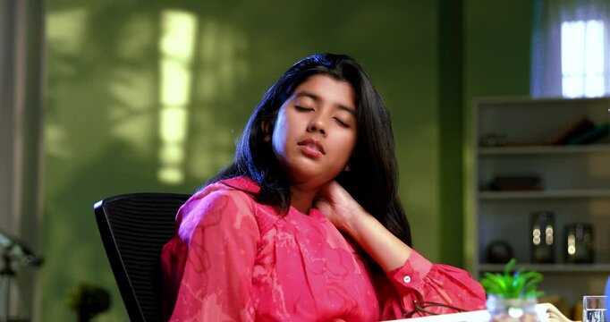 Indian Asian studious teenage beautiful girl sitting at study table in cozy lavish home, stretching hands, feeling tired, experiencing stiffness in her neck while studying, writing, showing fatigue