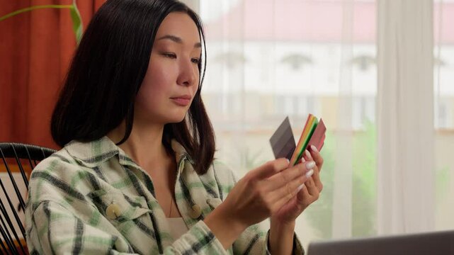 Asian Korean Chinese Japanese woman designer freelancer female girl indoor businesswoman shopping choosing color holding paper document colorful multicolored palette catalog buyer laptop business home