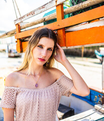 Caucasian woman model with blue eyes looking forward beach in the background, boats near 