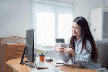 Obraz premium Young asian businesswoman is showing a gift box during a video call in her bright home office, working remotely and celebrating a special occasion
