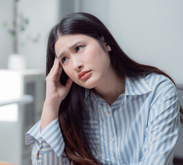 Young Asian business woman feeling tired and having headache in office after working on computer for a long time, she is touching her head, feeling stressed and suffering from office syndrome