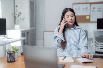 Fototapeta premium Businesswoman managing her office tasks, using a calculator and talking on the phone while working at her desk. Engaging in finance and communication in a modern, organized workspace