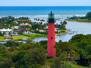 Jupiter Inlet Lighthouse: Iconic red lighthouse stands tall amidst a coastal landscape of lush greenery, serene water, and a vibrant sky, inviting exploration and reflection. © Mark