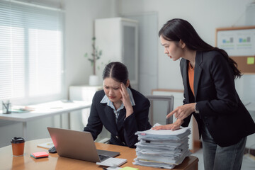 Asian businesswomen are having a discussion about paperwork at office desk, one of them is having a...