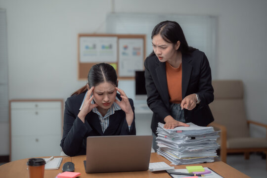 Asian businesswomen are working together in the office, but the boss is blaming her employee for poor performance, making her stressed and having a headache