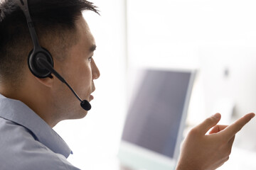 Serious Asian telemarketing employee man in headset talking to client at workplace. Support center...