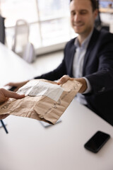 Male Internet store manager giving packet with ordered goods to customer, sitting at work table....