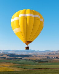 Naklejka premium Vibrant Yellow Hot Air Balloon Ascending Over Scenic Landscape Under Clear Blue Sky