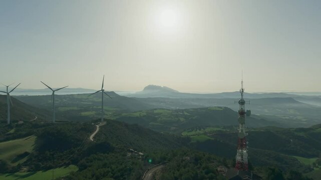Metraje a&eacute;reo en 4K de un parque e&oacute;lico al amanecer, con el sol proyectando un contraluz dorado. El dron avanza suavemente, mostrando aerogeneradores que generan energ&iacute;a renovable sobre colinas verdes
