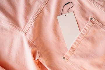 Blank white tag on pink denim jacket with metal buttons. Fashion label for branding or price....