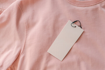 Blank white tag on pink cotton t-shirt. Empty label for branding or price, textile texture...