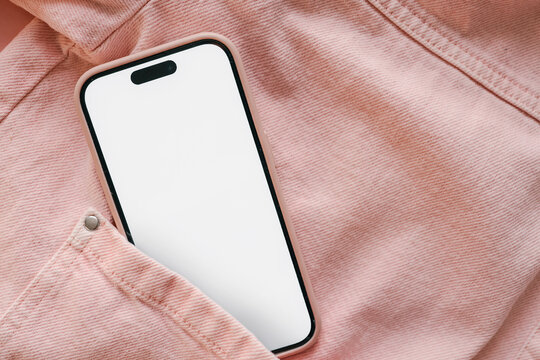 Modern smartphone with blank white screen in pocket of pink denim jacket. Mobile phone mockup. Fashion and technology concept. Close-up, flat lay, top view