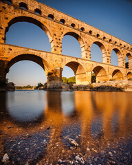 Pont du Gard, ancient Roman aqueduct bridge, Provence late afternoon golden light on arches mirroring in river, Gorges du Gardon, natural landscape designated Biosphere Reserve by UNESCO, France