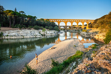 Pont du Gard, ancient Roman aqueduct bridge, Provence late afternoon golden light on arches mirroring in river, Gorges du Gardon, natural landscape designated Biosphere Reserve by UNESCO, France