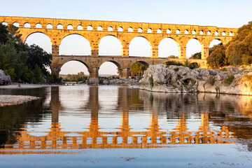 Pont du Gard, ancient Roman aqueduct bridge, Provence late afternoon golden light on arches mirroring in river, Gorges du Gardon, natural landscape designated Biosphere Reserve by UNESCO, France