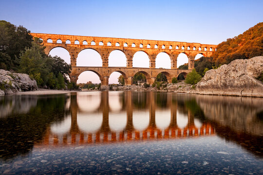 Pont du Gard, ancient Roman aqueduct bridge, Provence sunset light on arches mirroring in river, Gorges du Gardon, natural landscape designated Biosphere Reserve by UNESCO, France